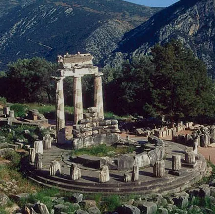 The ruins of the sanctuary at Delphi, with three standing columns of the tholos below a mountainside.