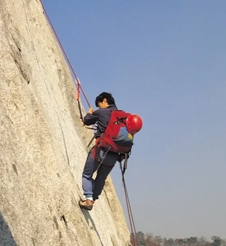 A climber part way up a steep dam wall on ropes, carrying a pack.