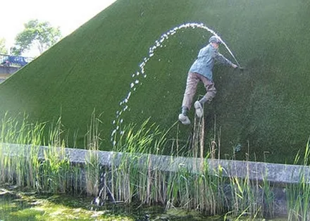 A man standing on a grassy dyke, plugging a jet of water bursting from the bank with his hand.